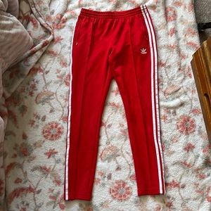 Red adidas workout pants, white stripes on the sides and zippers on the ankles